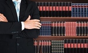 Close-up Of Male Lawyer With Arm Crossed Standing In Front Of Book Shelf